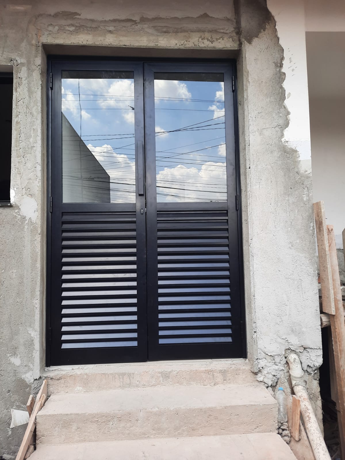 Porta de alumínio preta com veneziana e vidro instalada em obra.